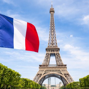 The Eiffel Tower stands tall under a bright blue sky, with the French national flag waving prominently in the foreground, symbolizing France's authority over its domestic regulations—including its recent order to ISPs to block access to Polymarket.