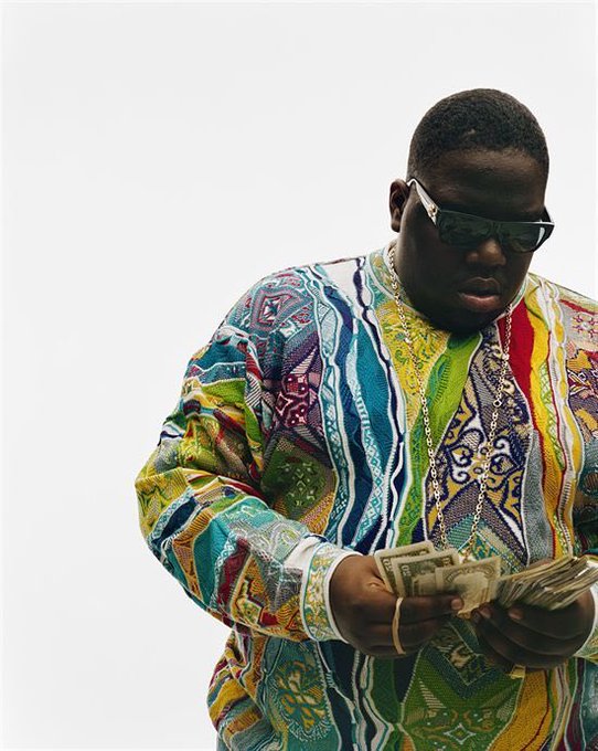 A man wearing sunglasses and a colorful patterned shirt counting a stack of US dollar bills.