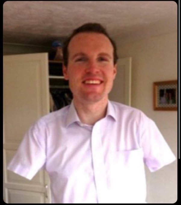 Casual photo of a smiling man in a light purple/lavender short-sleeve button-up shirt, photographed indoors in what appears to be a home setting.