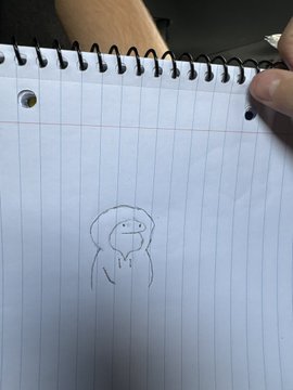 A small pencil sketch in a spiral notebook depicting a simple, cartoonish figure with a wide smile and short legs.