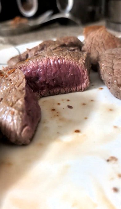 Slices of medium-rare steak rest on a white plate, showing a pink interior with browned edges.