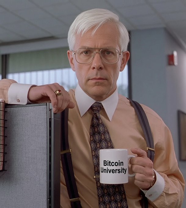 An older man with white hair and glasses wearing suspenders holds a mug labeled 'Bitcoin University' while leaning on a cubicle wall.