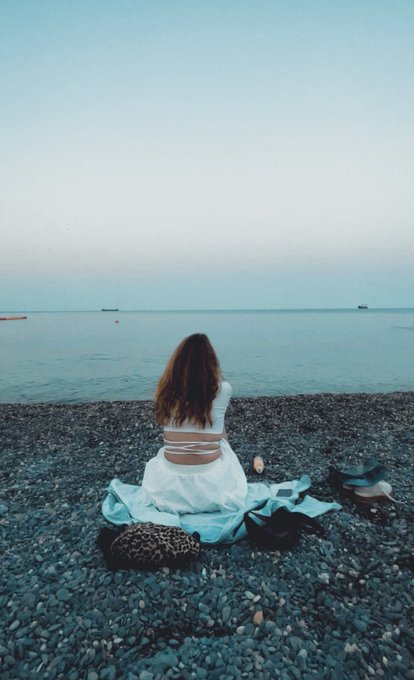 A young woman with long brown hair sits alone on a rocky shore, gazing out at a calm sea during what appears to be twilight. The image evokes the contemplative, introspective mood of the accompanying poem, which speaks to being a meaningful presence in someone's life before the moment passes.

The visible text reads: "133xtz" alongside an objkt.com token link, indicating this is an NFT artwork listing.