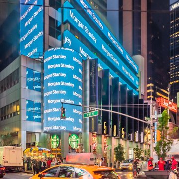 A Morgan Stanley building is illuminated at night with multiple "Morgan Stanley" logos displayed across its facade, alongside a sign showing "155 W 42 St," representing the financial firm whose increased holdings in iShares Bitcoin Trust and iShares Ethereum Trust ETFs are highlighted in the accompanying news.