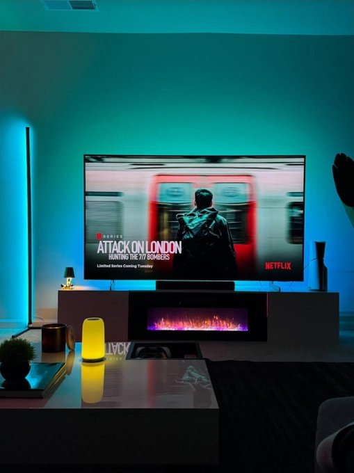 A living room scene with cyan ambient lighting features a large TV displaying 'ATTACK ON LONDON' from Netflix, positioned above a modern electric fireplace.