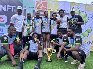 Group photo of a football/soccer team posing with a trophy and medals at what appears to be an 'MNCHAIN SUMMIT FOOTBALL' event, with players in dark uniforms and a 'NFT' banner visible.