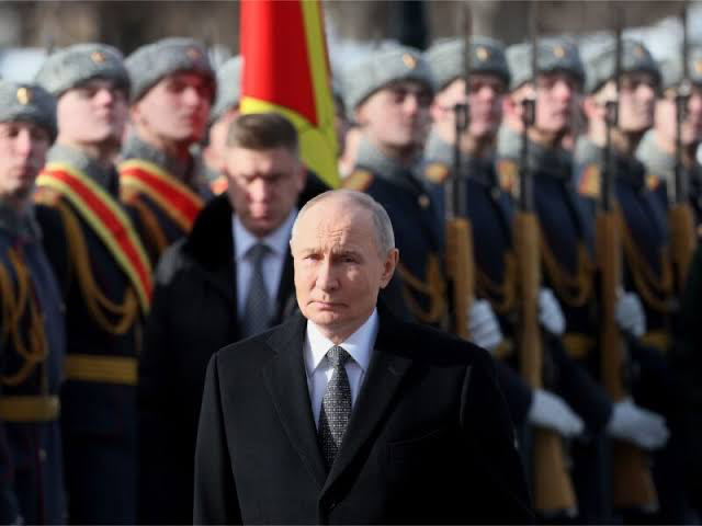 Vladimir Putin stands solemnly in front of a formation of Russian honor guard soldiers in uniform during what appears to be a formal military ceremony. The image accompanies the breaking news about European nations issuing warnings of intensifying Russian hybrid threats and potential strikes against NATO.