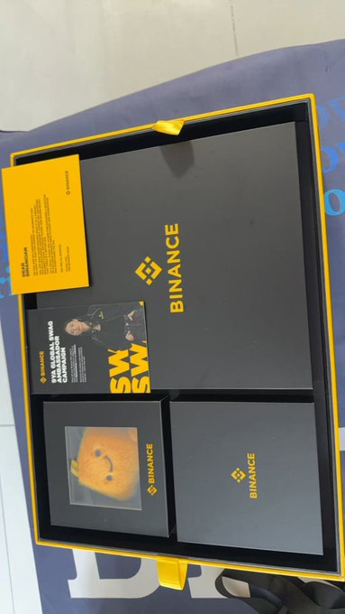 A Binance 7th Anniversary limited edition gift box (币安七周年限定礼盒) is displayed, featuring branded black and yellow items including a card, a "SWSW" themed brochure with CZ's photo, and merchandise, matching the celebratory unboxing post.