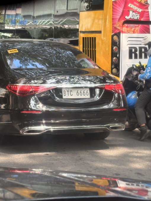 A black Mercedes-Benz S560 with the license plate 'BTC 6666' stopped in traffic, alongside a yellow vehicle and a motorcyclist.