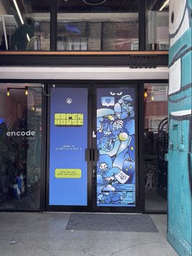 A photograph of a storefront with blue double doors covered in colorful cartoon stickers, located in a building marked "encode."