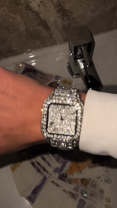 A person's wrist rests on the edge of a white porcelain sink, showcasing an opulent diamond-encrusted watch, with British pound banknotes scattered on the surface below, visually reinforcing the post's theme of $ANSEM reaching a $5 billion market cap through imagery of immense wealth.