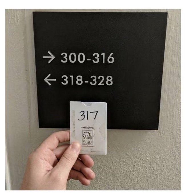 A hand holds up a key card labeled "317" with a "Sukı Sunul" logo in front of a black wall sign indicating rooms 300-316 are to the right and 318-328 are to the left, humorously suggesting the key holder has wandered into the wrong area.