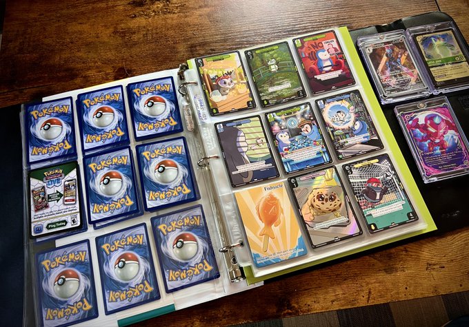 An open three-ring binder resting on a wooden surface, filled with Pokémon trading cards in protective sleeves, including various holographic and full-art cards.