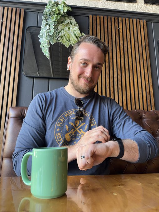 The image features a man sitting at a table with his arm resting on a chair while wearing sunglasses and holding a green coffee cup. The background includes a wooden wall, which adds to the overall ambiance of the scene. There are also some plants in the room that contribute to the atmosphere. The post seems to be a message or quote about friendship, as it references "i thought leaving wallchain would tell me who my friends were." This implies that the man's friends might not have been present at this particular moment captured in the image.