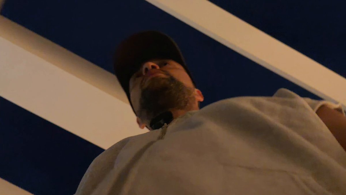 The image shows a man wearing a white shirt, standing against a blue background with white stripes. He has a beard and appears to be looking up at something or someone above him. The caption below the photo reads "MAJOR $XRP ALERT NOW!!!!!!!!". This suggests that there is an important announcement related to cryptocurrency in progress.
