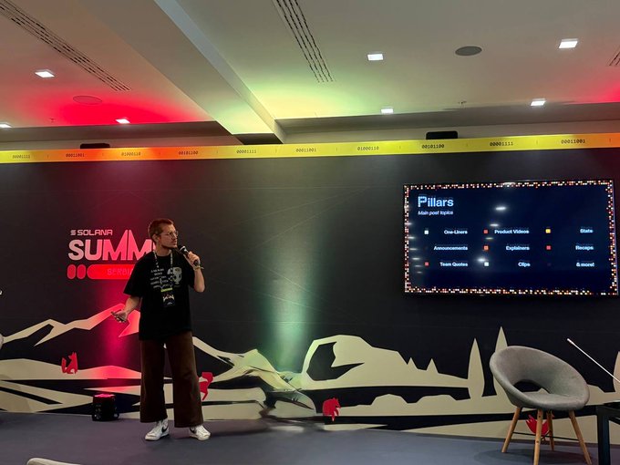 A presenter speaks into a microphone at the Solana Summit in Serbia, with a slide behind him titled "Pillars" detailing "Main pool topics" including One-Liners, Product Videos, Data, Announcements, Explainers, Memes, Team Quotes, Clips, and Rewards. The scene captures one of his talks mentioned in the post, with the branded "#SOLANASUMMIT" backdrop and a demo day presentation stage visible.