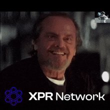 The image features a man with a beard, wearing a black jacket, smiling at the camera. Below him, there's text that reads "XPR Network", which appears to be related to the content of the image or possibly an advertisement for the network. The focus on this text suggests that it might be a promotional piece or a statement about the XPR Network.