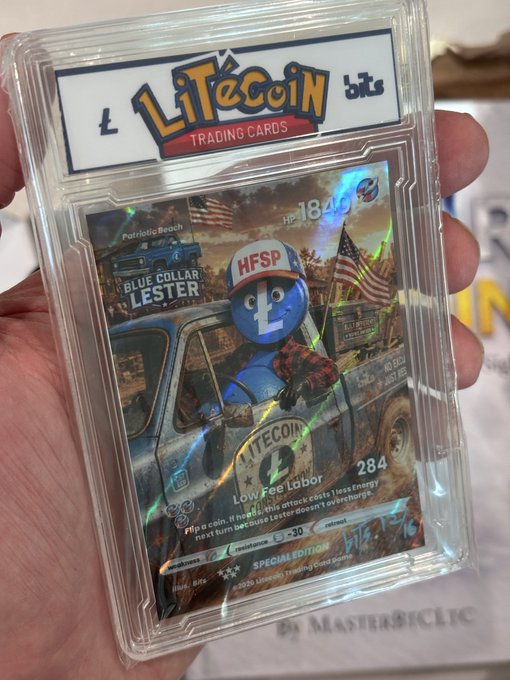 A Litecoin trading card in a protective case featuring a character called 'BLUE COLLAR LESTER' with 'Low Fee Labor' stats and a handwritten signature dated '5/18/25'.