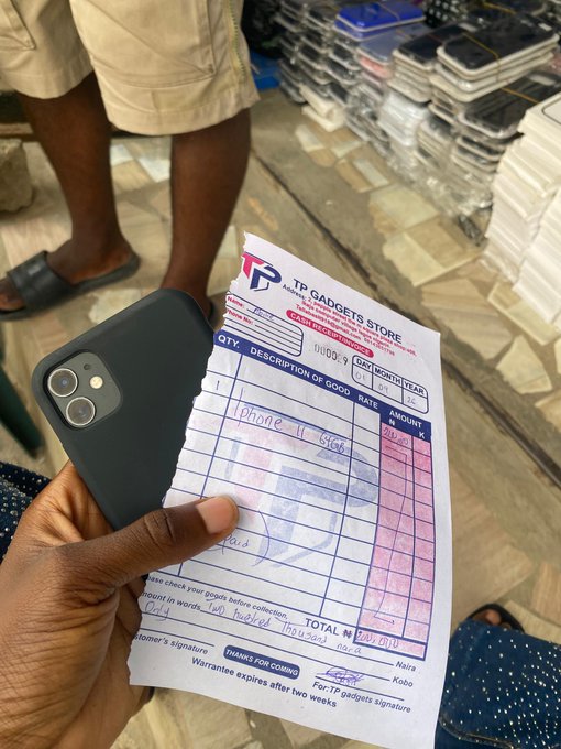 A hand holds an iPhone with a dark case alongside a printed receipt from 'TP GADGETS STORE' in Asaba, Nigeria, detailing a sale of an iPhone 11 for 450,000 Naira.