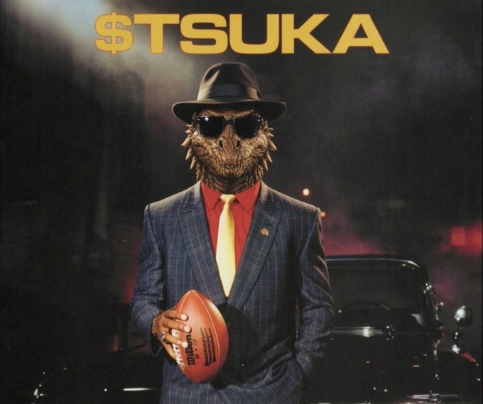 A stylized poster features a figure in a pinstripe suit, red shirt, yellow tie, and fedora with a dinosaur head and sunglasses, holding a football, with the text "$TSUKA" in yellow at the top.