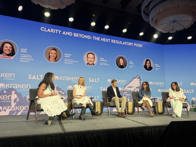 A photograph of a panel discussion at a conference sponsored by Kraken and SALT, with panelists including Allie Page, Kristin Smith, Miles Jennings, and Julie Stitzel under the banner 'CLARITY AND BEYOND: THE NEXT REGULATORY PUSH'.