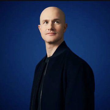 A portrait of a bald man in a dark jacket against a blue background.