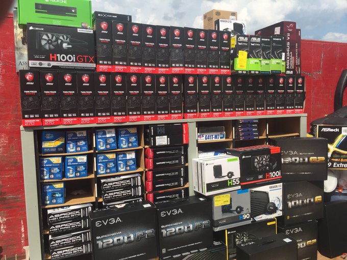 A display of computer hardware components including Corsair power supplies (H100iGTX), MSI Radeon graphics cards, EVGA SuperNOVA power supplies (1200P2, 1000W), and various CPUs and motherboards stacked on shelves at what appears to be a retail or wholesale location.