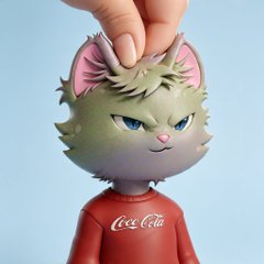 A hand pinches the tufted hair of a stylized green cat figurine wearing a red Coca-Cola shirt, showcasing a 3D-rendered NFT character with an unamused expression that fits the playful "paperhands" rescue theme mentioned in the post.