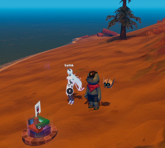 A video game scene showing two characters, 'Luna' and another figure, standing on a sandy cliff overlooking the ocean with a flag marker nearby.