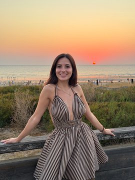 A woman in a striped dress posing on a wooden railing with a beautiful ocean sunset behind her.