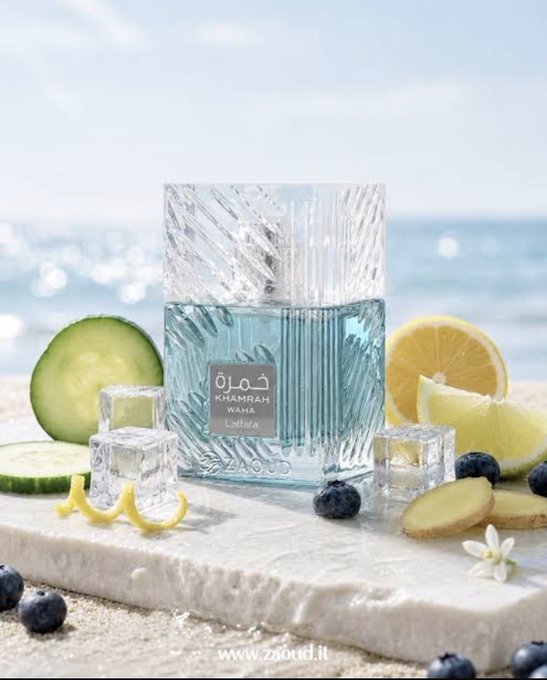 A product photo of a square, textured light blue perfume bottle labeled 'KHAMRAH WAHÀ Lattafa' by ZAQUD, placed on a stone slab surrounded by cucumber slices, ice cubes, blueberries, and lemon wedges with the ocean in the background.