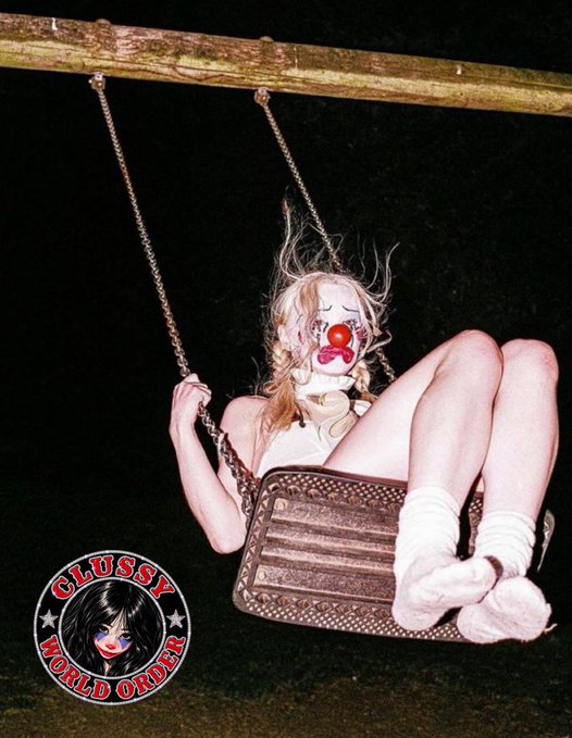 A person dressed as a clown sits on a swing at night, with a logo in the corner reading 'CLUSSY WORLD ORDER' featuring a stylized face.
