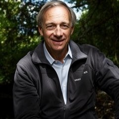 Ray Dalio, founder of Bridgewater Associates, smiles warmly in an outdoor portrait wearing a dark Helly Hansen fleece jacket. The image accompanies his commentary on the anticipated decline of fiat currencies and the rising importance of alternative stores of value like gold and Bitcoin.