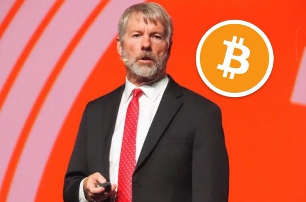 Michael Saylor, Executive Chairman of MicroStrategy and prominent Bitcoin advocate, stands on stage in a dark suit and red tie beside a large orange Bitcoin logo, delivering a keynote presentation aligned with the post's message about his lifelong and even posthumous commitment to BTC, underscoring Bitcoin as more than just a financial investment but a lasting legacy.