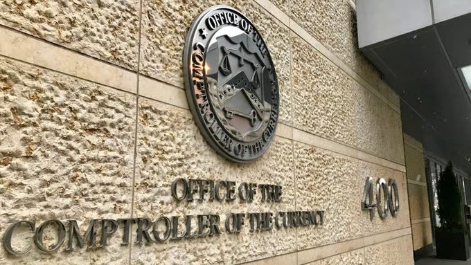 The exterior entrance of the "Office of the Comptroller of the Currency" building, featuring its circular bronze seal mounted on a textured stone wall alongside the address number 400.