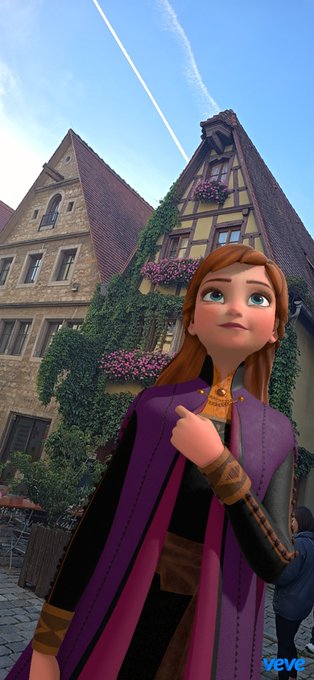 A 3D animated character resembling Anna from Frozen stands in front of traditional half-timbered European buildings under a blue sky with contrails.