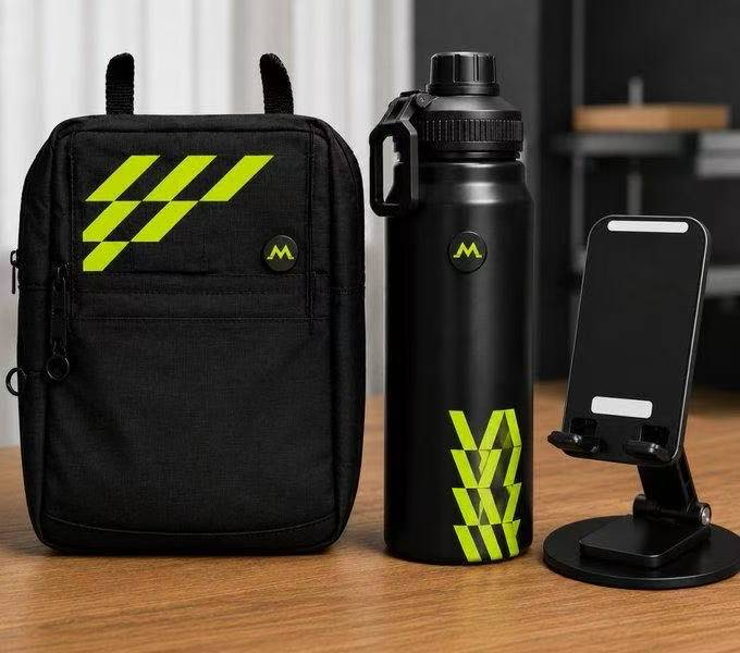 A product display on a wooden surface features a black backpack, a black water bottle, and a black phone stand, all branded with bright green 'M' logos and chevron patterns.