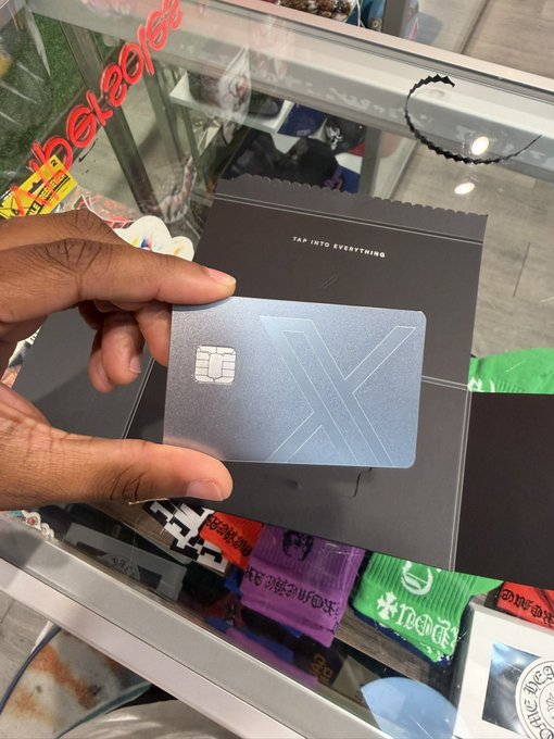 A hand holds a sleek black 'X' branded payment card from Banxe with the slogan 'TAP INTO EVERYTHING' displayed on its packaging.