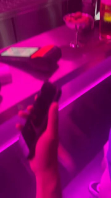 iced tea with a straw and a glass of water on a pink countertop, accompanied by a black phone and a silver tray.
