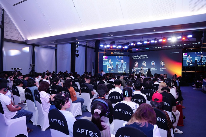 An audience wearing white APTOS shirts attends a cybersecurity panel titled "Crypto Cyber Security: The Jack & the Doom 1st" with speakers shown on screens.