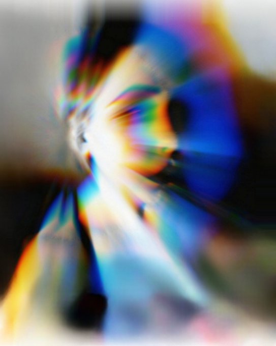 A heavily distorted, abstract image features an eye surrounded by a radial burst of rainbow colors and glitch effects.