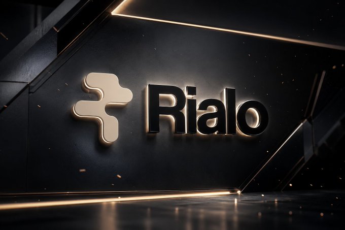 A sleek black 3D-rendered design displays the "Rialo" logo with a stylized cross-shaped icon, illuminated by warm gold accent lighting against a dark architectural background. The visual reinforces the post's message by presenting a polished, high-tech brand identity for a protocol that bridges on-chain ownership with off-chain privacy for real-world assets.