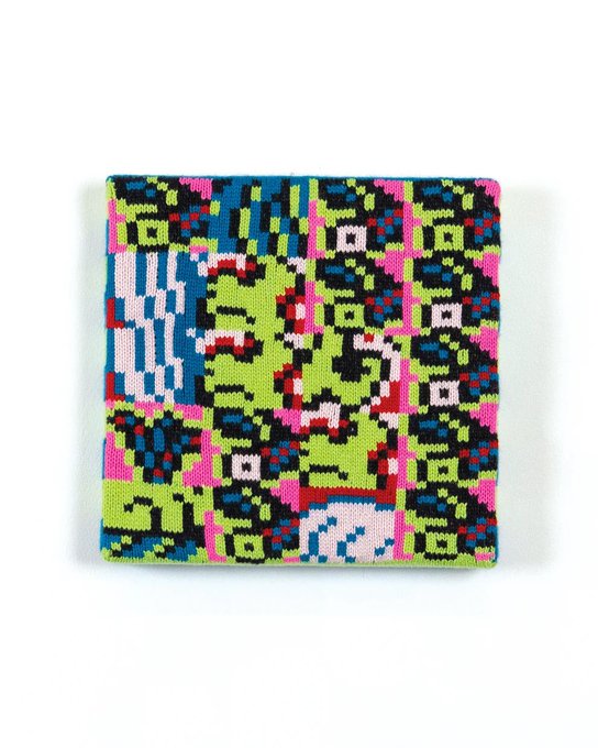 A square piece of fabric or embroidery with a colorful, pixelated, glitch-art style pattern featuring green, blue, pink, and black.