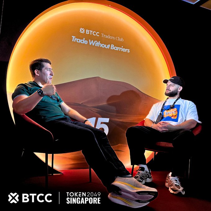 Two men sit in red chairs on a stage at TOKEN2049 Singapore, with a BTCC "Trade Without Barriers" backdrop behind them, discussing crypto trading. The image ties into the post's promotion of an XRP giveaway on the BTCC platform, with the sponsor logos and event branding visible at the bottom.