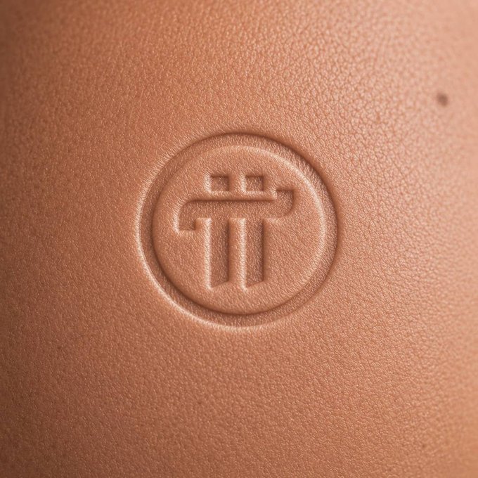 A close-up of a tan leather surface featuring an embossed circular logo with a stylized geometric design resembling a gate or arch.