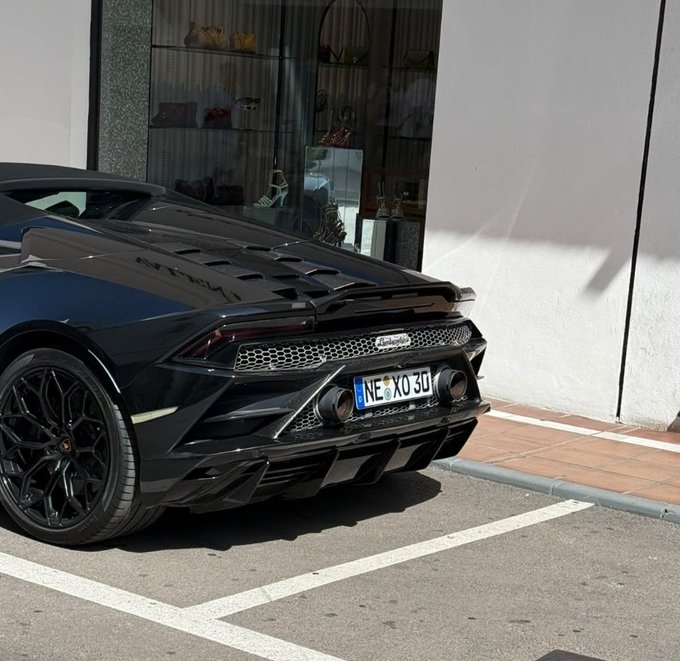 The rear view of a black Lamborghini Huracán parked on a street, featuring a custom license plate reading 'NE XO 30' and prominent quad exhaust pipes.