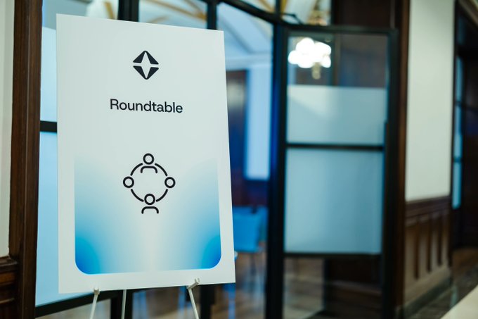 A sign on an easel reading 'Roundtable' with a logo, displayed in what appears to be an office or conference area with glass doors.