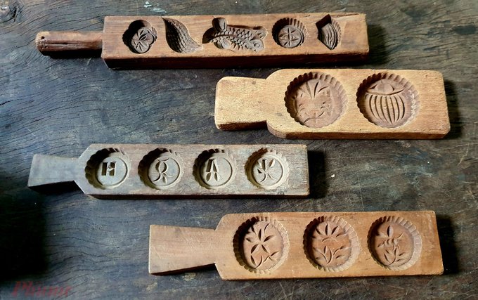 Four hand-carved wooden molds rest on a rustic wooden surface, each featuring various decorative impressions including fish, flowers, leaves, and Chinese characters, traditionally used for shaping mooncakes or other festive pastries.