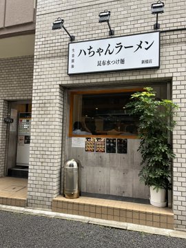 The exterior of a Japanese ramen shop named '八ちゃんラーメン' is shown with a white signboard above the entrance, tiled walls, and a small potted plant by the door.
