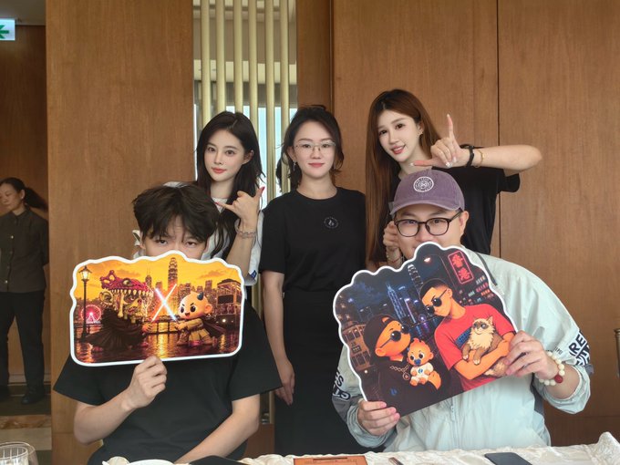 A group of five people pose for a photo, with two individuals in front holding illustrated character cutouts and three women standing behind them.